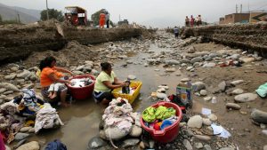 Residents do the laundry at a flooded Ramiro Priale highway, after rivers breached their banks due to torrential rains, causing flooding and widespread destruction in Huachipa, Lima, Peru
