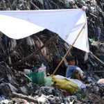 A boy rests in the shade while waiting for his father to salvage items from a garbage dump in Denpasar.