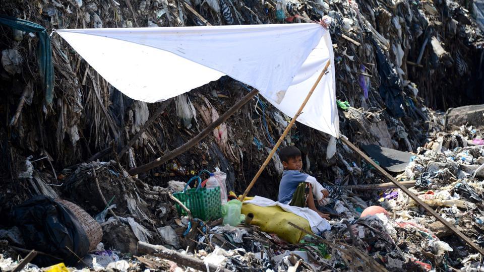 A boy rests in the shade while waiting for his father to salvage items from a garbage dump in Denpasar.
