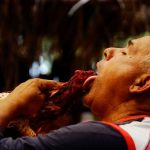 A cockfighting enthusiast uses his tongue to clean the blood of his rooster during a fight at a cockfighting arena in Moron