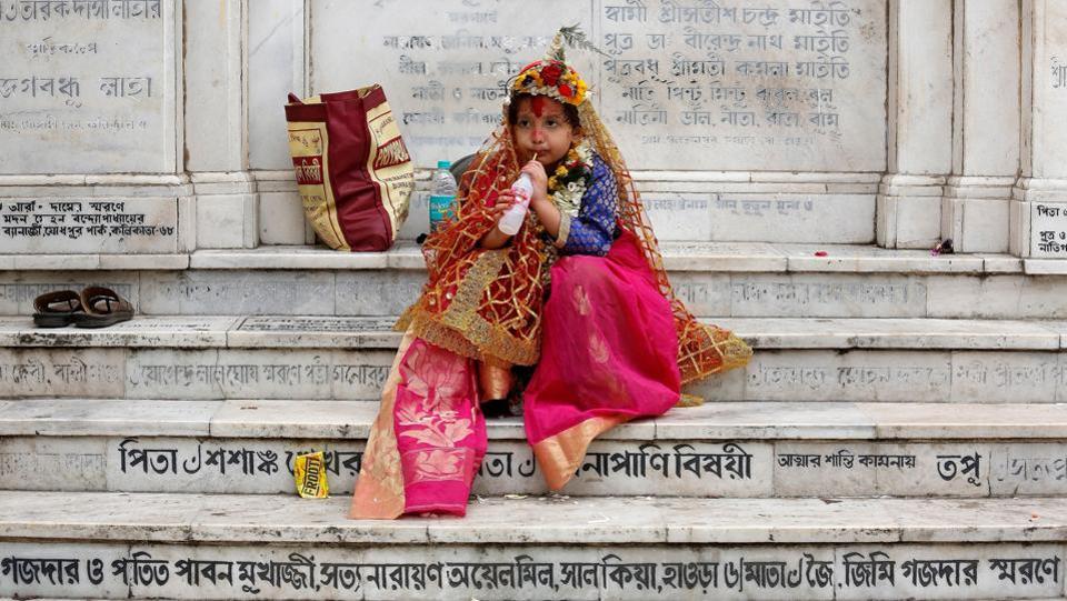 A girl dressed as Kumari, sipping a soft drink as she sits on stairs after attending rituals to celebrate the Navratri Festival inside the Adyapeath Temple, on the outskirts of Kolkata