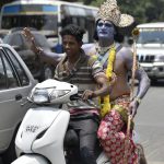 An artist dressed as Lord Ram rides pillion on a scooter before a road show on the occasion 9th day of Navratri at a Hanuman Temple near Kempegowda Railway Station in Bengaluru on Wednesday, April 5, 2017