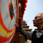 An artist paints on the giant wheel of the chariot of God Bhairab