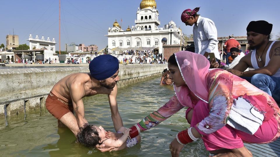 Sikh devotees hold a child as they take a dip in the holy sarovar at Gurudwara Bangla Sahib in New Delhi