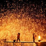Performers throw molten iron against a wall to create sparks.