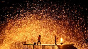 Performers throw molten iron against a wall to create sparks.