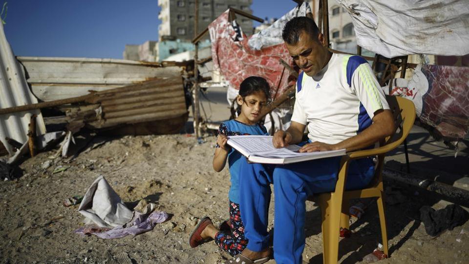 A Palestinian man reads a copy of the Quran, to a young girl at Al-Shatee refugee camp in Gaza City.