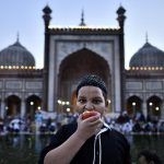 A boy takes a bite from an apple with the Jama Masjid in the backdrop after iftar on the eve of Juma-tul-Wida, on June 22, 2017 in New Delhi, India