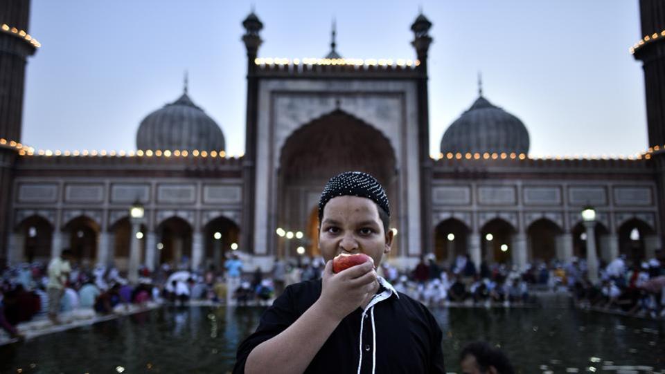 A boy takes a bite from an apple with the Jama Masjid in the backdrop after iftar on the eve of Juma-tul-Wida, on June 22, 2017 in New Delhi, India