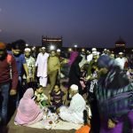 A family sits down at iftar time as a swarm of people moves around them at Old Delhi’s Jama Masjid