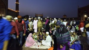 A family sits down at iftar time as a swarm of people moves around them at Old Delhi’s Jama Masjid