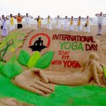 Some people practice yoga near a sand sculpture by artist Manas Sahoo on the eve of International Day of Yoga at a beach in Puri, Odisha, on June 20, 2017