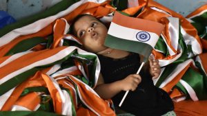 A little girl holds on to a national flag, laying in a heap of tricoloured ribbon as other family members are busy completing orders at a flag making workshop in Old Delhi.