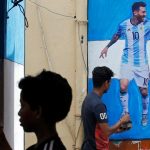 A boy paints a wall with the colours of Argentina's flag next to a man giving finishing touches to a cut-out of soccer player Lionel Messi.