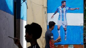 A boy paints a wall with the colours of Argentina's flag next to a man giving finishing touches to a cut-out of soccer player Lionel Messi.