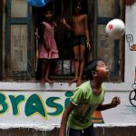 A boy plays in front an image of Brazil's Neymar painted on a wall in an alley