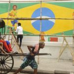 A hand-rickshaw puller moves past a wall painted with graffiti of Brazilian football players Neymar and Marcelo