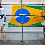 A painter applies finishing touches to an image of Neymar on a large Brazilian flag on a road side wall.