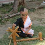 An Indian child dressed as Mahatma Gandhi sits with a wooden charkha or spinning wheel at the lawns of the Gujarat Vidhyapith to commemorate the 150th Birthday of Mahatma Gandhi in Ahmedabad on October 1, 2018. - Gandhi Jayanti or Birthday of Mahatma Gandhi is celebrated on October 2 every year.