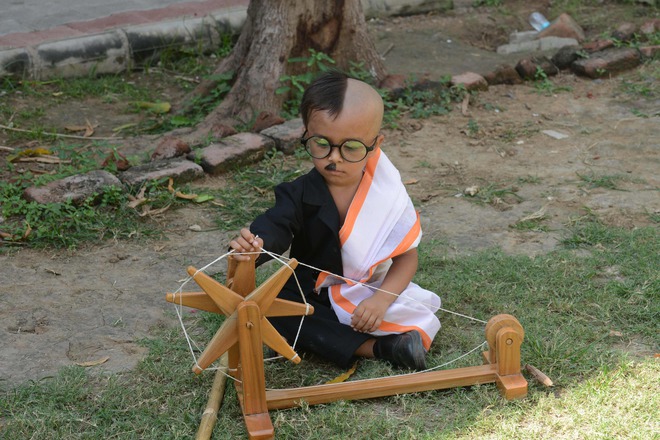 An Indian child dressed as Mahatma Gandhi sits with a wooden charkha or spinning wheel at the lawns of the Gujarat Vidhyapith to commemorate the 150th Birthday of Mahatma Gandhi in Ahmedabad on October 1, 2018. - Gandhi Jayanti or Birthday of Mahatma Gandhi is celebrated on October 2 every year.