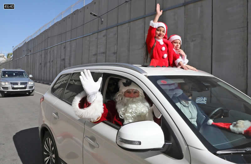 A family dressed as Santa Claus drive behind the convoy of Apostolic Administrator of the Latin Patriarchate of Jerusalem Pierbattista Pizzaballa along Israel’s controversial separation barrier in the occupied West Bank town of Bethlehem on December 24, 2019.