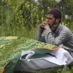A close relative sits next to a deceased COVID-19 before burial at Zawoora on the outskirts of Srinagar on May 4, 2021