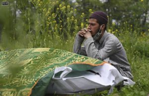 A close relative sits next to a deceased COVID-19 before burial at Zawoora on the outskirts of Srinagar on May 4, 2021